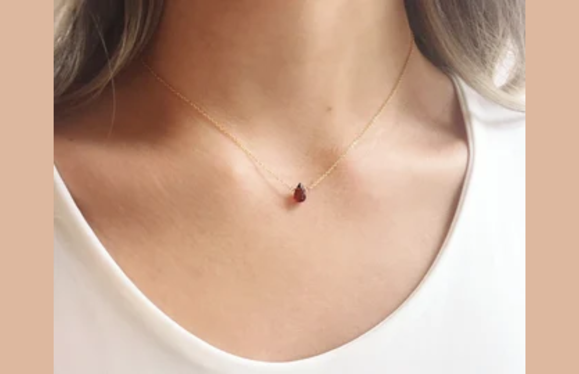 A teardrop-shaped gem with several facets hangs on a delicate necklace on a girl wearing a white shirt