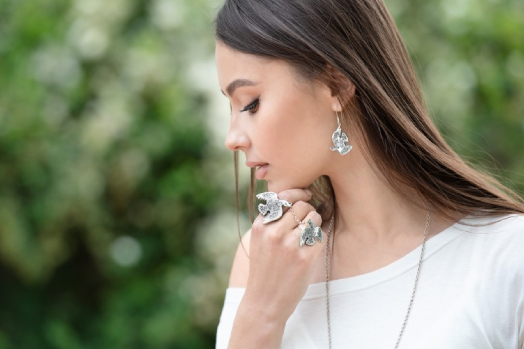 A woman wearing a plain white shirt and silver rings, necklace, and earrings