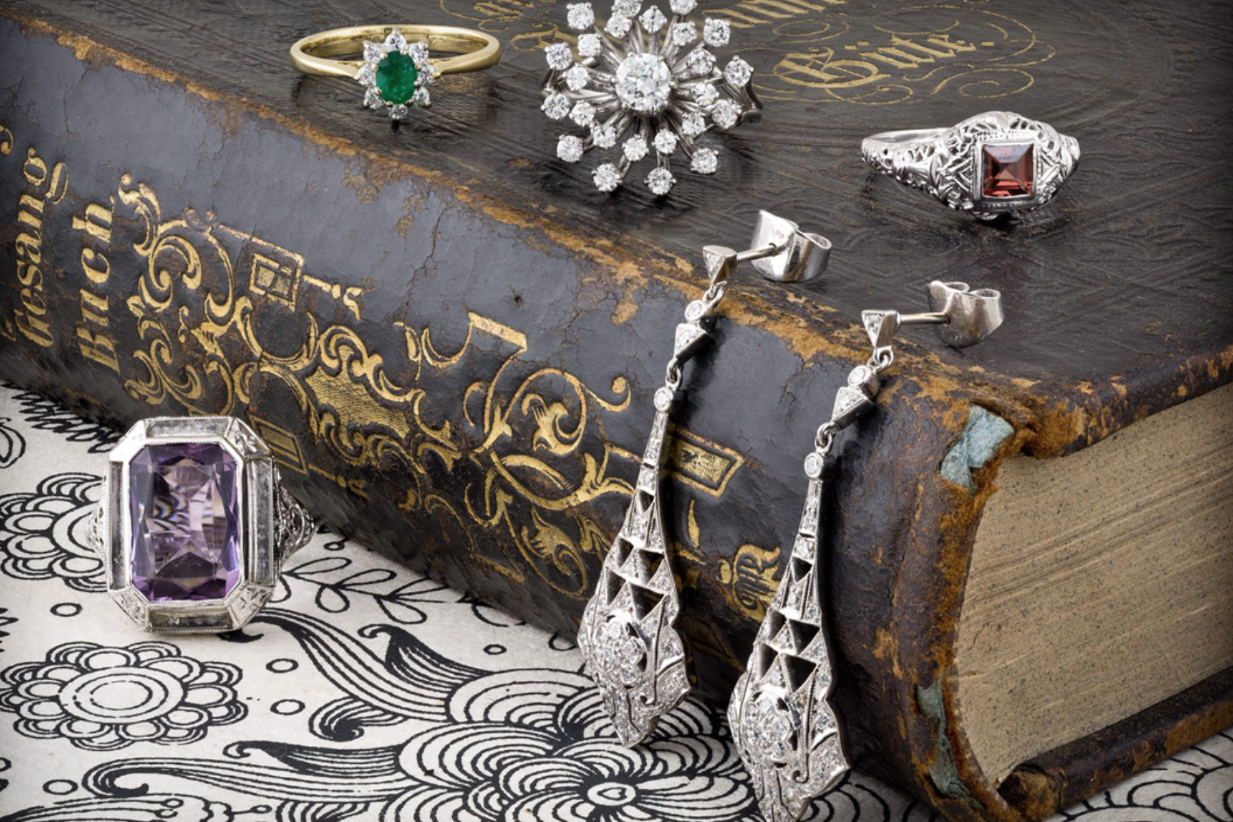 Various pieces of art deco vintage jewelry adorn the top and sides of an old large book