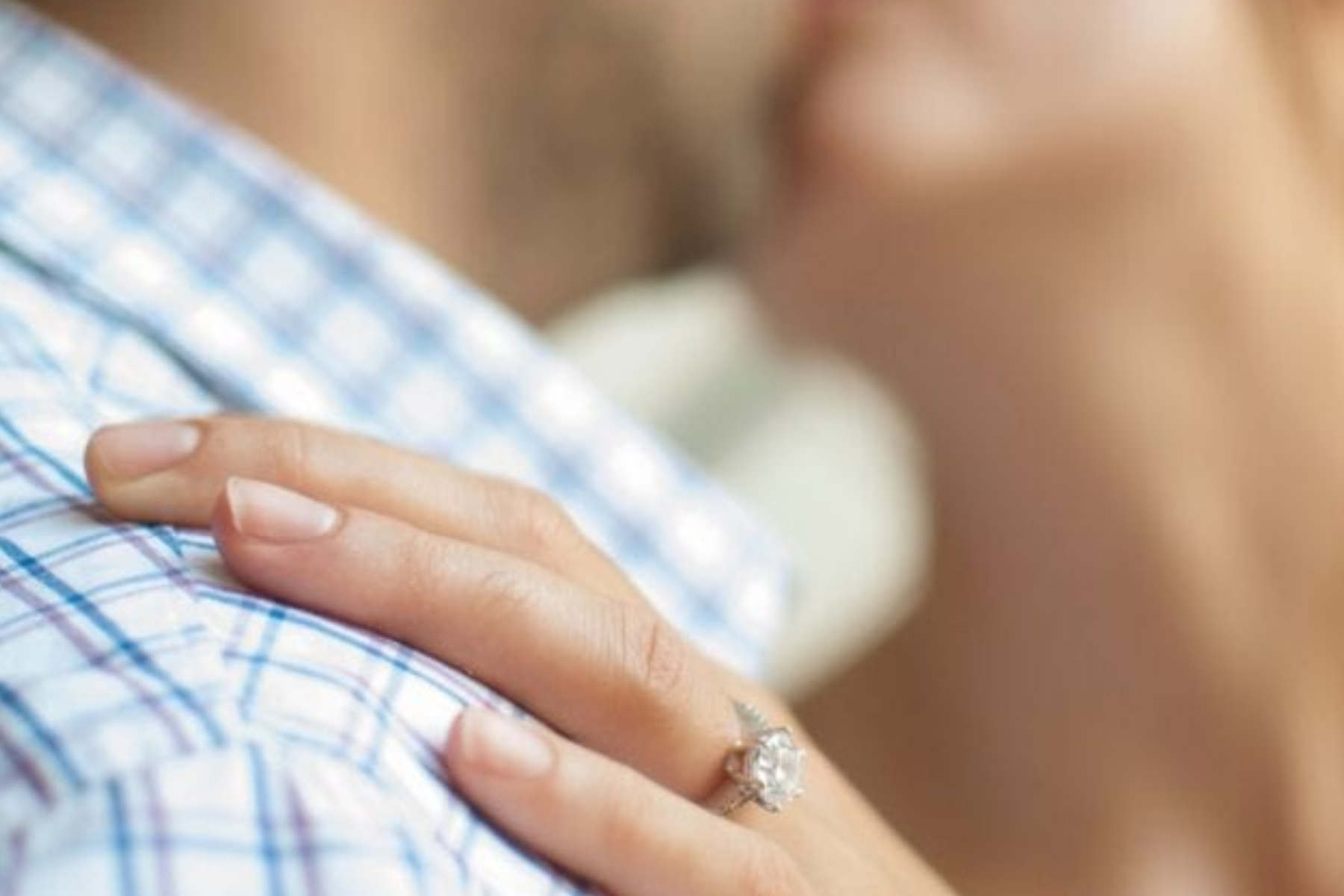 A newly engaged couple kissing while the halo engagement ring on the woman's ring finger is highlighted