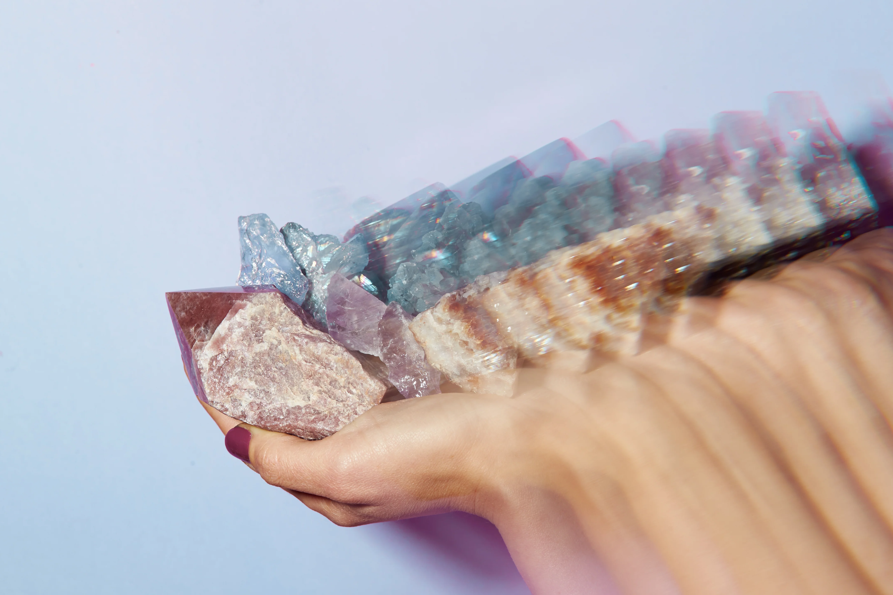 A close-up photograph of a woman's hand holding a gemstone. The background is blurred, creating a soft and dreamy effect