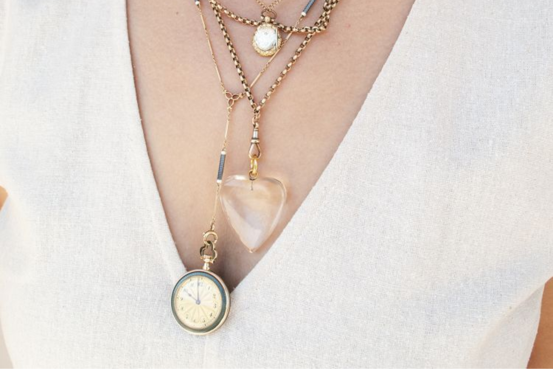 A female individual donning a white shirt adorned with a combination of vintage and modern necklaces
