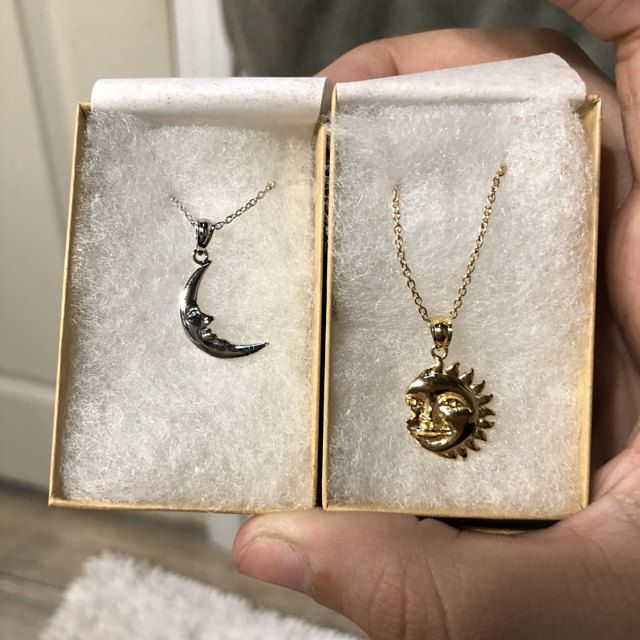 Two jewelry boxes, one containing a silver moon necklace and the other containing a diamond necklace, held in the hand of an individual