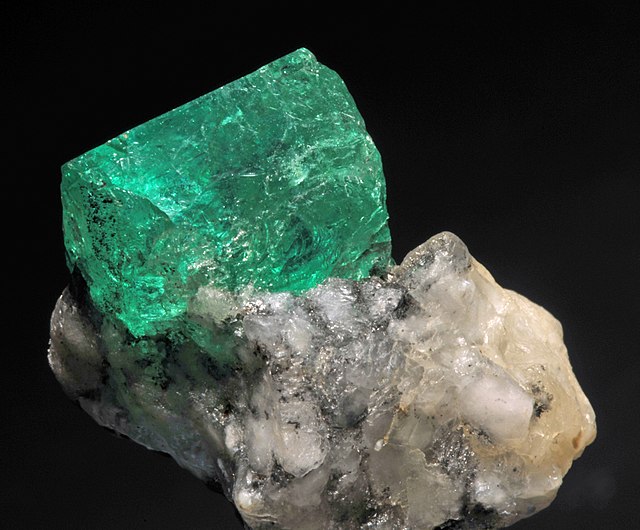 The emerald stone is still attached to its host, a transparent rock