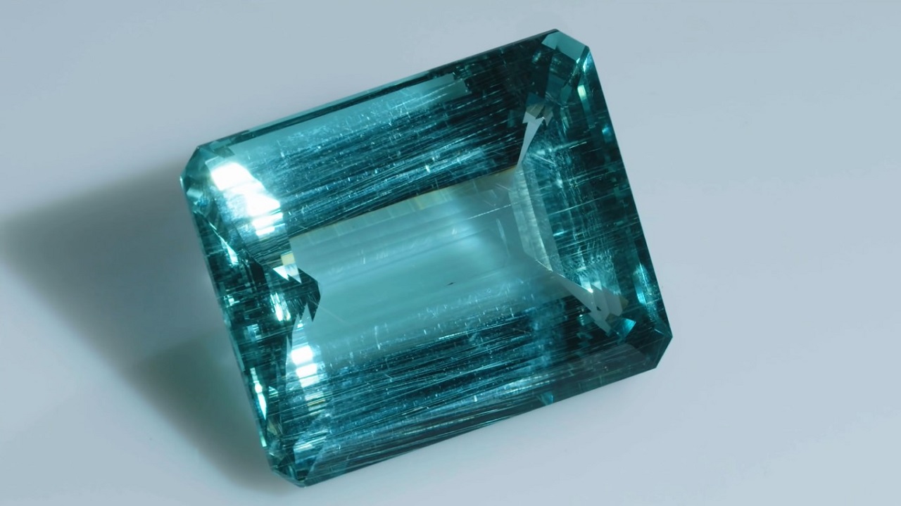 A faceted emerald-cut aquamarine casting a small shadow, with luster seen from its upper right corner.