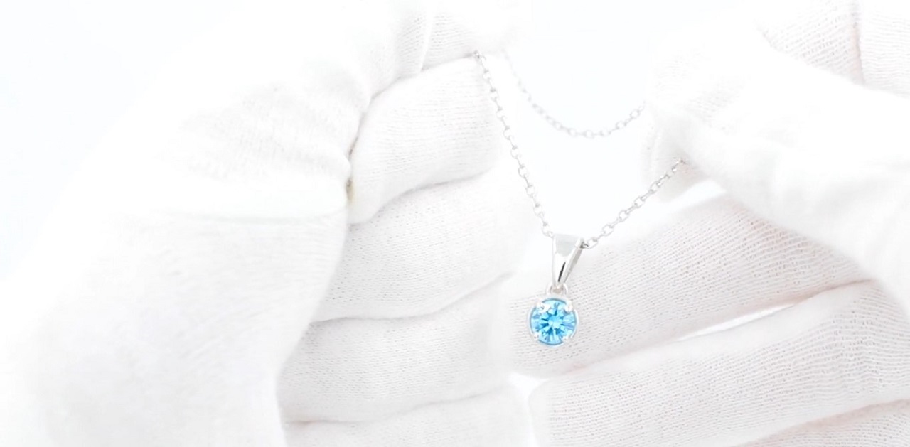 A sterling silver necklace and a pendant with a round teal zircon held by hands in white cotton gloves